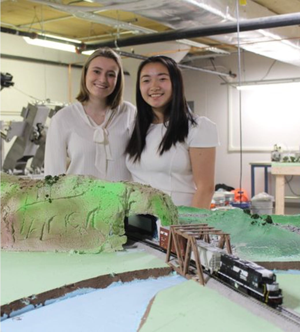 two students stand behind a train set